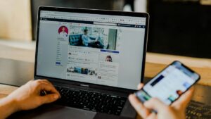 Ondernemer bekijkt een Facebook-bedrijfspagina op een laptop en houdt tegelijk een smartphone vast